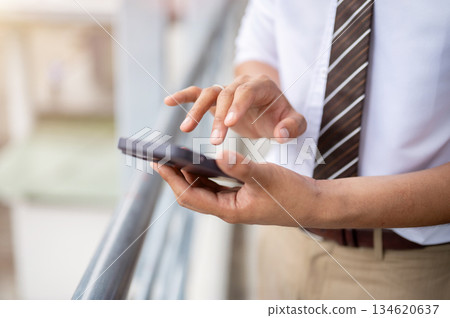 Close up businessman or office worker holding and typing on phone standing on pedestrian footbridge. Close up businessman or office worker holding and typing on phone standing on pedestrian footbridge. 134620637
