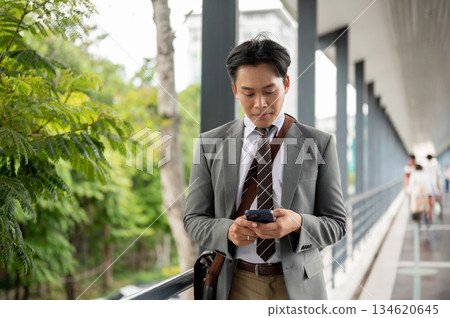 Businessman or office worker holding and looking at phone chatting with family on pedestrian footbridge. Businessman or office worker holding and looking at phone chatting with family on pedestrian footbridge. 134620645