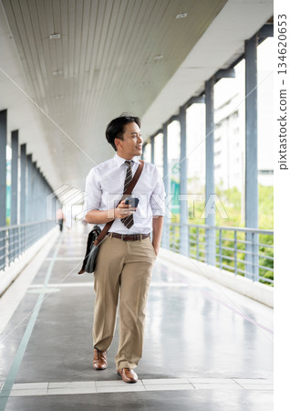 Businessman or office worker holding a phone looking around while walking on a pedestrian footbridge 134620653