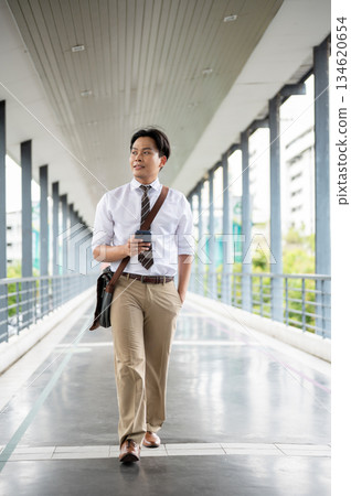 Businessman or office worker holding smartphone looking around as walking on a pedestrian footbridge Businessman or office worker holding smartphone looking around as walking on a pedestrian footbridge 134620654