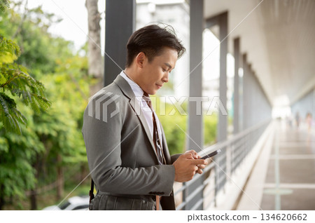 Businessman or office worker holding looking at phone chatting with family on pedestrian footbridge. Businessman or office worker holding looking at phone chatting with family on pedestrian footbridge. 134620662