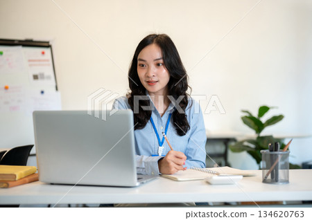 Female office worker or businesswoman writing in notebook with pencil while sitting at working table Female office worker or businesswoman writing in notebook with pencil while sitting at working table 134620763