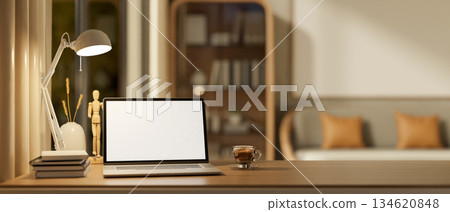 Blank screen laptop with books and a glass of coffee under lamp light on wooden table in living room Blank screen laptop with books and a glass of coffee under lamp light on wooden table in living room 134620848