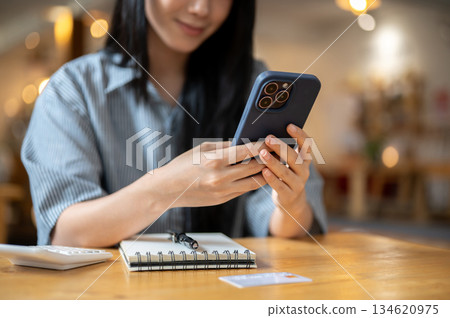 Close up of woman hands holding phone watching video or texting over notebook on cafe wooden table. Close up of woman hands holding phone watching video or texting over notebook on cafe wooden table. 134620975