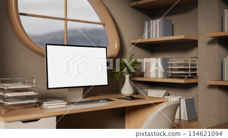 Blank screen computer on wooden study table aside bookshelf under oval window in modern living room. Blank screen computer on wooden study table aside bookshelf under oval window in modern living room. 134621094