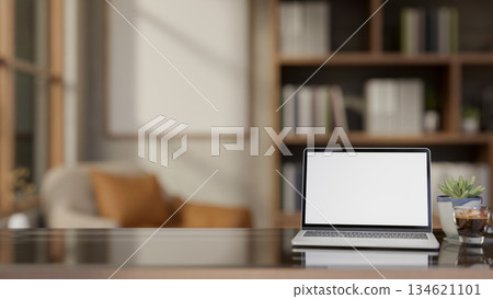 White screen laptop aside coffee and potted plant on glass top wooden table in living room or cafe. 134621101
