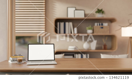 White screen laptop and glass of coffee with books on wooden table in living room with stylish shelf 134621119
