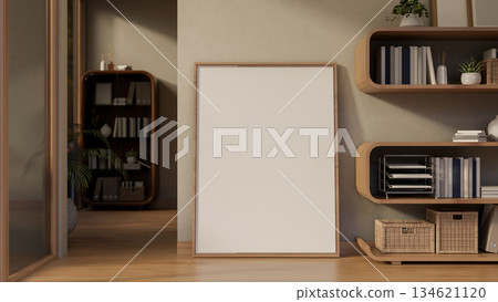 Blank frame on parquet floor leaning against wall next to stylish bookshelf in modern living room. 134621120