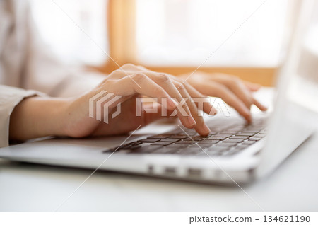 Close up pair of hands typing both hands on laptop keyboard at white table beside glass wall in cafe 134621190