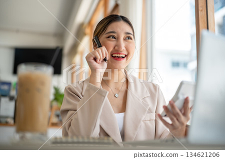 Asian woman holding pen and calculator thinking while sitting with laptop and coffee at cafe's table Asian woman holding pen and calculator thinking while sitting with laptop and coffee at cafe's table 134621206