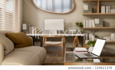 White screen laptop with books on glass top wooden table and fabric sofa in a bedroom or living room 134621376