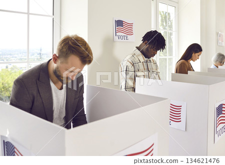 American citizens standing at vote center in voting booth putting ballots in bin on election day. 134621476