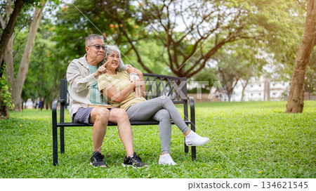 Glasses old man hugging pointing to woman while sitting leaning against each other on bench in park. 134621545