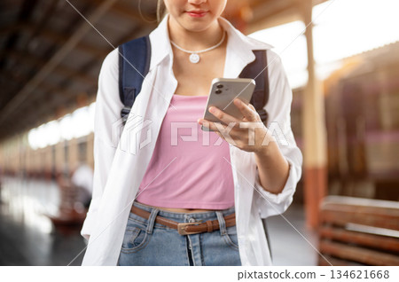 Close up woman with bag holding and looking at smartphone while standing or walking at train station Close up woman with bag holding and looking at smartphone while standing or walking at train station 134621668