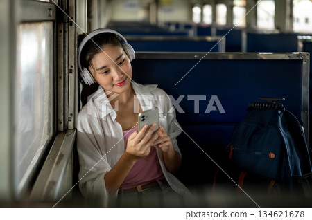 Asian woman with headphone listening to music from phone sitting on carriage bench at train station. 134621678