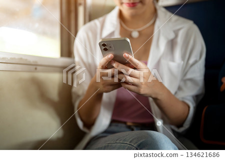 Close up of woman holding phone with both hand looking or typing as sitting on train carriage bench. Close up of woman holding phone with both hand looking or typing as sitting on train carriage bench. 134621686
