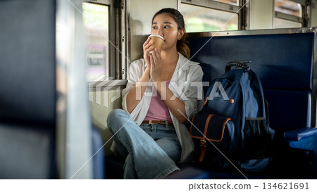 Pretty asian woman holding coffee drinking or sipping as sitting on carriage bench at train station. Pretty asian woman holding coffee drinking or sipping as sitting on carriage bench at train station. 134621691