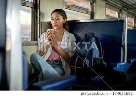 Pretty asian woman holding coffee looking or blowing as sitting on carriage bench at train station. 134621692