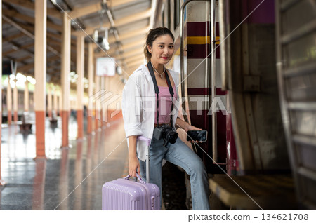 Asian woman with camera holding phone and luggage as walking into carriage at train station platform 134621708