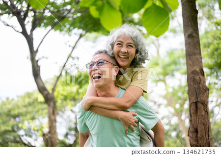 Glasses old man laughing as carrying smiling old woman on his back while standing or walking in park 134621735