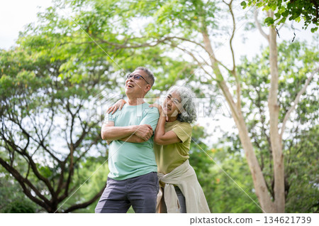 Old woman clinging or holding onto glasses old man's shoulder while standing on grass lawn in park. Old woman clinging or holding onto glasses old man's shoulder while standing on grass lawn in park. 134621739
