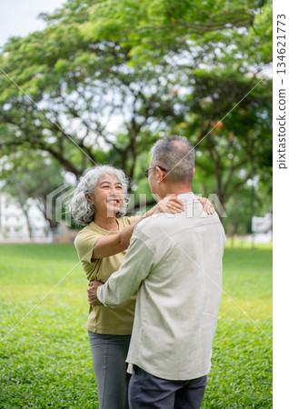 Old woman smiling and holding onto her old man shoulder while dancing together on grass lawn in park Old woman smiling and holding onto her old man shoulder while dancing together on grass lawn in park 134621773