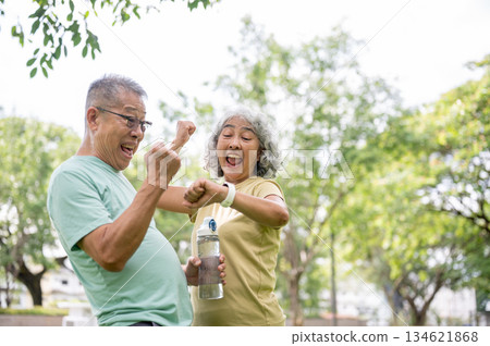 Old man and woman making a fist looking excited at wristwatch after finish exercise in time at park. Old man and woman making a fist looking excited at wristwatch after finish exercise in time at park. 134621868