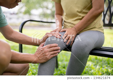 Old man holding or massaging a pained or injury knee of a woman sits on bench after exercise in park Old man holding or massaging a pained or injury knee of a woman sits on bench after exercise in park 134621874