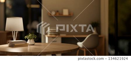 Books aside lamp on round wooden table with blurred background of a living room or bedroom at night. Books aside lamp on round wooden table with blurred background of a living room or bedroom at night. 134621924