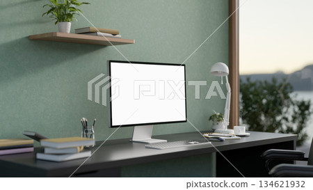 White screen computer with lamp and books on black table in a green wall room with scenery outside. 134621932