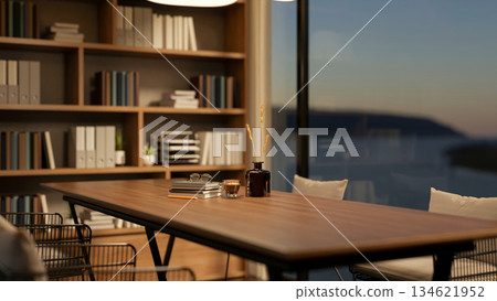 Glass of coffee and book on wooden table with armchairs beside bookshelf in a living room or library 134621952