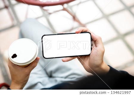 Hand holding coffee and white screen smartphone horizontally watching video playing game on bench. 134621997