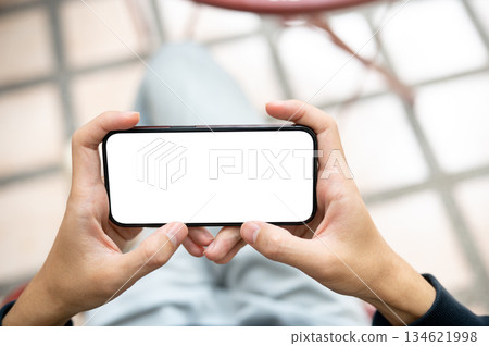 Close up hands holding blank screen smartphone horizontally watching videos or playing game on bench 134621998