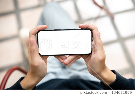 Close up hands holding white screen smartphone horizontally watching videos or playing game on bench 134621999