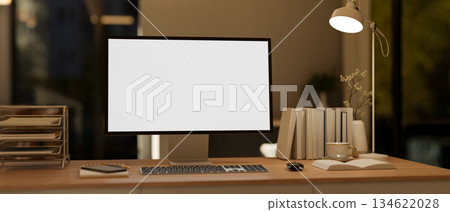 White screen computer with books and aside lamp on wooden table in a dim lit living room or bedroom. 134622028