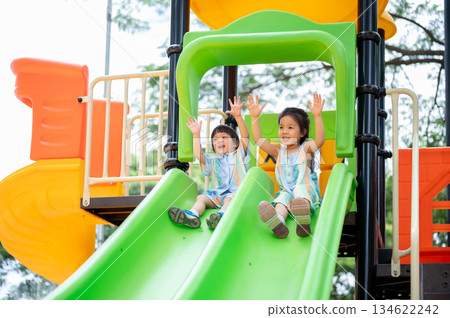 Asian girl and boy siblings happily playing on a colorful climbing slides in the park's playground. Asian girl and boy siblings happily playing on a colorful climbing slides in the park's playground. 134622242