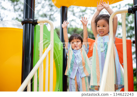 Asian girl and boy siblings standing playing on a colorful climbing slide in the park's playground. Asian girl and boy siblings standing playing on a colorful climbing slide in the park's playground. 134622243
