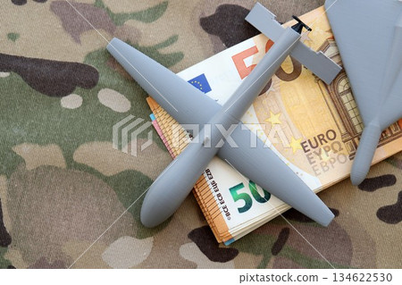 Unnamed grey toy drones and Euro bills stack on camouflage fabric close up. Drone manufacturing funds Unnamed grey toy drones and Euro bills stack on camouflage fabric close up. Drone manufacturing funds 134622530