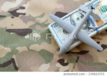 Unnamed grey toy drone model and dollar bills on camouflage fabric close up. Drone manufacturing funds Unnamed grey toy drone model and dollar bills on camouflage fabric close up. Drone manufacturing funds 134622555