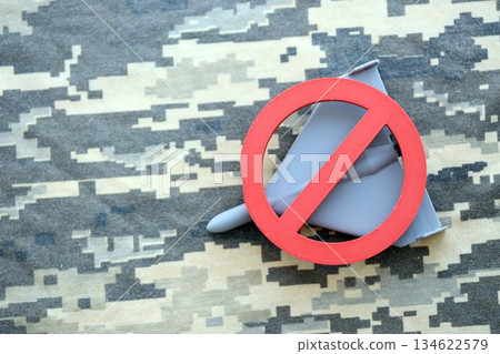 Unnamed grey toy drone and red prohibition sign on camouflage fabric close up. Anti-aircraft warfare concept 134622579