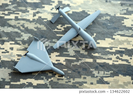 Unnamed grey toy drones models on camouflage fabric close up. Kamikaze drone and observation drone Unnamed grey toy drones models on camouflage fabric close up. Kamikaze drone and observation drone 134622602
