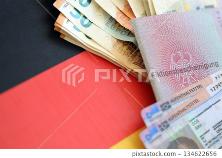 German Permanent resident card and document specimen with euro money bills lies on Germany flag close up. Aufenthaltstitel and Fiktionsbescheinigung 134622656