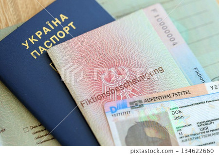 German Permanent resident card and document specimen lies with Ukrainian passport on wooden table close up. Aufenthaltstitel and Fiktionsbescheinigung German Permanent resident card and document specimen lies with Ukrainian passport on wooden table close up. Aufenthaltstitel and Fiktionsbescheinigung 134622660