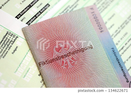German temporary Permanent resident card specimen lies on german tax form close up. Fiktionsbescheinigung and einkommensteuererklarung German temporary Permanent resident card specimen lies on german tax form close up. Fiktionsbescheinigung and einkommensteuererklarung 134622671
