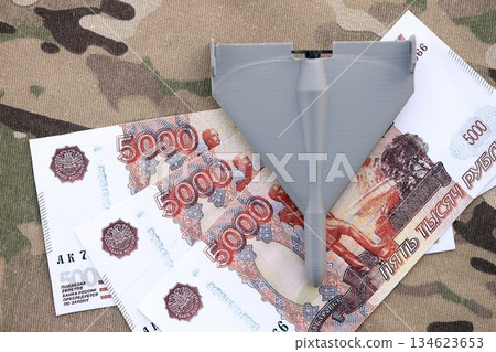Russian money with bullets and kamikaze drone on multicam camouflage fabric close up. Concept of russian army funds and invasion to Ukraine Russian money with bullets and kamikaze drone on multicam camouflage fabric close up. Concept of russian army funds and invasion to Ukraine 134623653