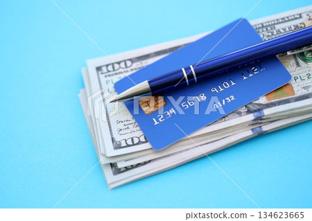 Credit card and pen with US dollar currency money bills banknotes on light blue background. Business, financial operations and accounting in United States of America 134623665