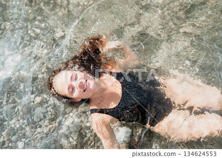 Smiling Woman in Black Swimsuit Floating in Clear Water Smiling Woman in Black Swimsuit Floating in Clear Water 134624553