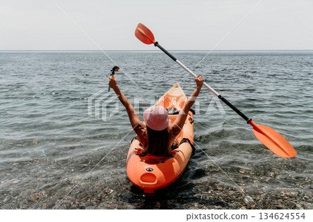 Kayaking Woman Paddle Ocean - A woman enjoys kayaking in a calm ocean, raising her paddle in the air. 134624554