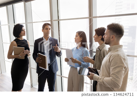Team listening boss standing in office against panoramic window Team listening boss standing in office against panoramic window 134624711