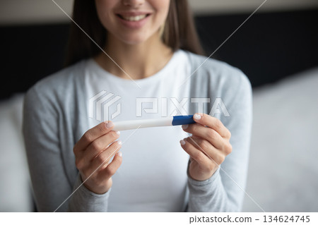 Closeup happy smiling young woman holding pregnancy test in hands Closeup happy smiling young woman holding pregnancy test in hands 134624745
